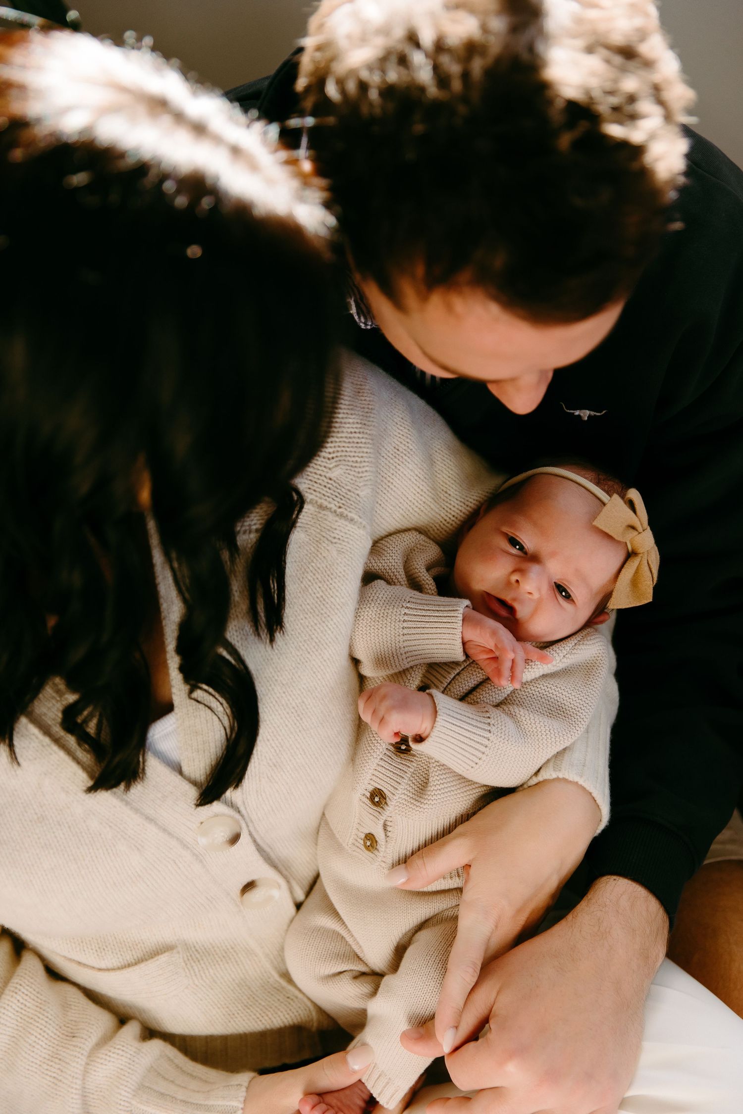 Tender family moment as parents cuddle with their baby wearing a knit hat and cream-colored outfit.