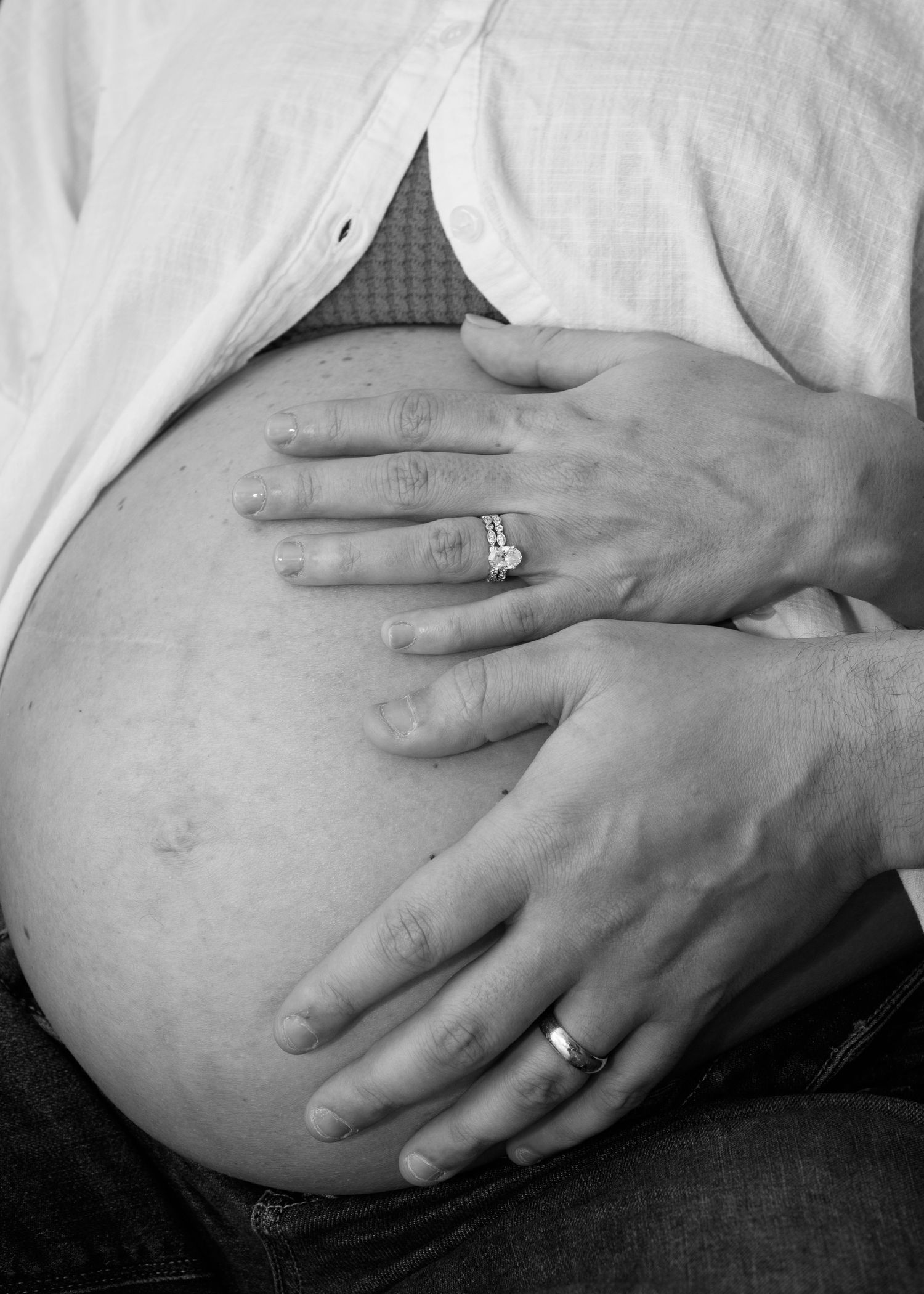 A tender black and white portrait of a new father gently snugging his sleeping baby wearing a white bow headband in Charleston SC.