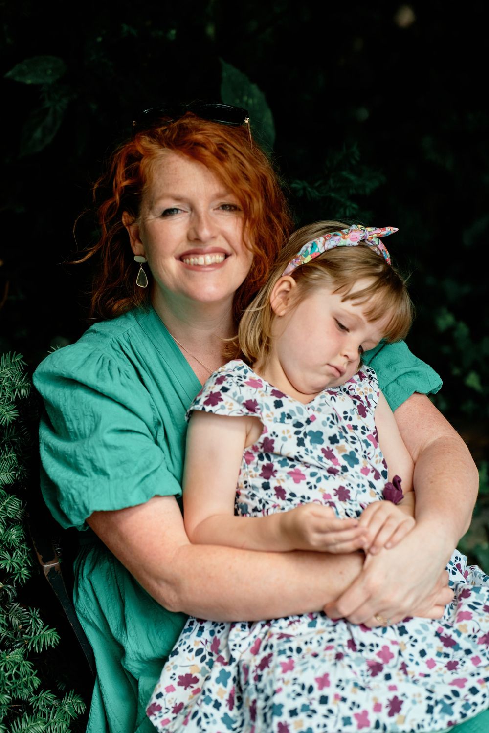 Tender moment between a woman in green and small girl in floral dress against dark background.