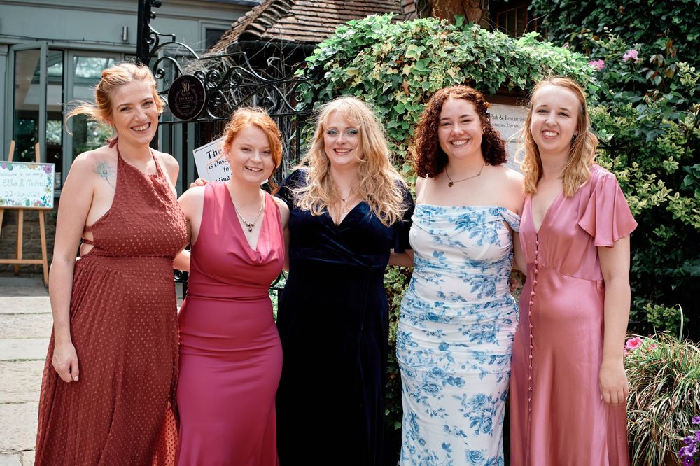 A group wearing various shades of pink and floral dresses stands together at an outdoor gathering.