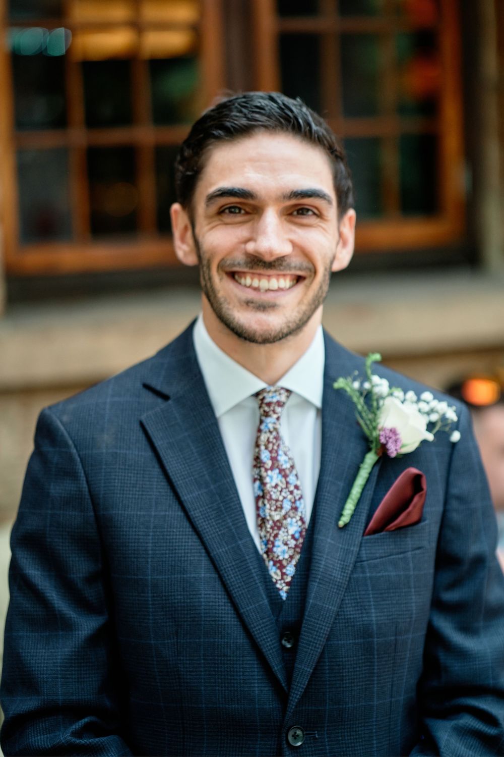 Groom in navy suit and floral tie shows progression of smiling poses across four connected portrait photos.