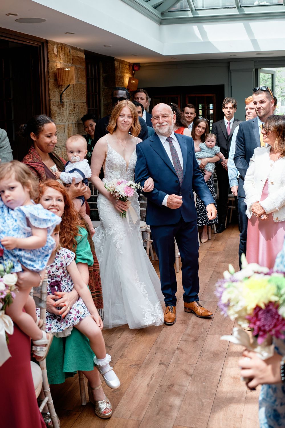 Wedding ceremony at an indoor venue with hardwood floors and skylight as guests look on from both sides of the aisle.