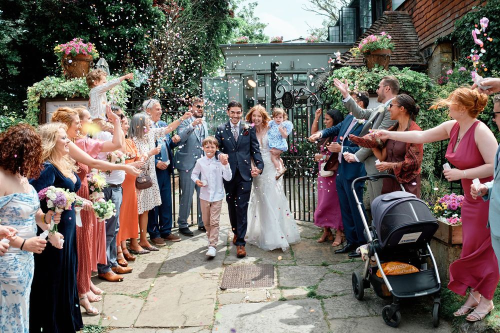 A wedding celebration with guests gathered outdoors throwing confetti and flower petals in a joyful moment.