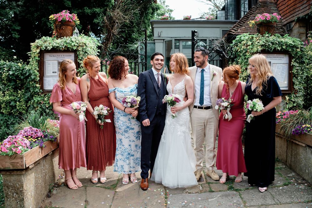 Wedding party poses together in a garden setting with beautiful floral arrangements and greenery.