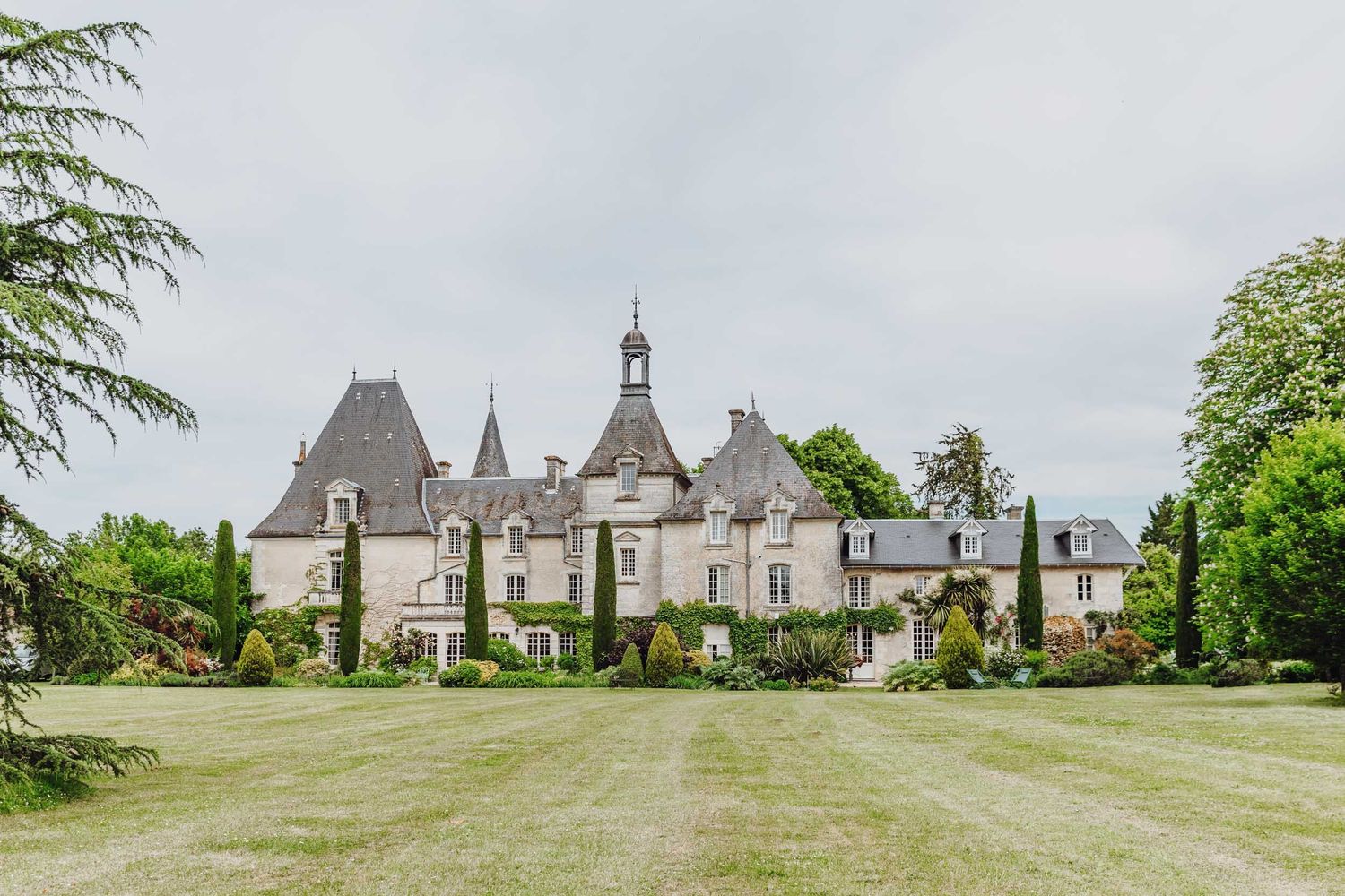 Elegant French chateau with pointed turrets and gray stone architecture stands majestically on a manicured green lawn.