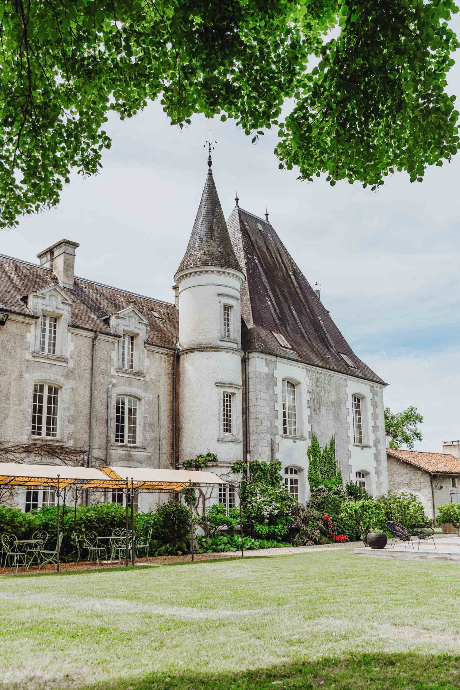 A panoramic view of a French chateau with traditional stone architecture and well-manicured lawn surrounded by trees.