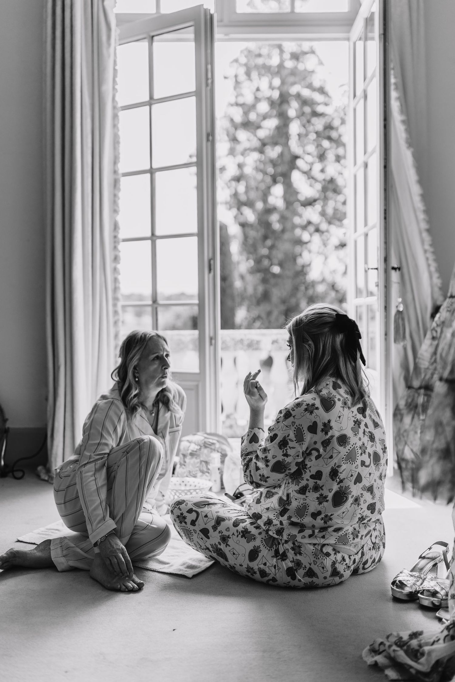 Two friends sit on the floor by an open window sharing an intimate conversation in black and white.
