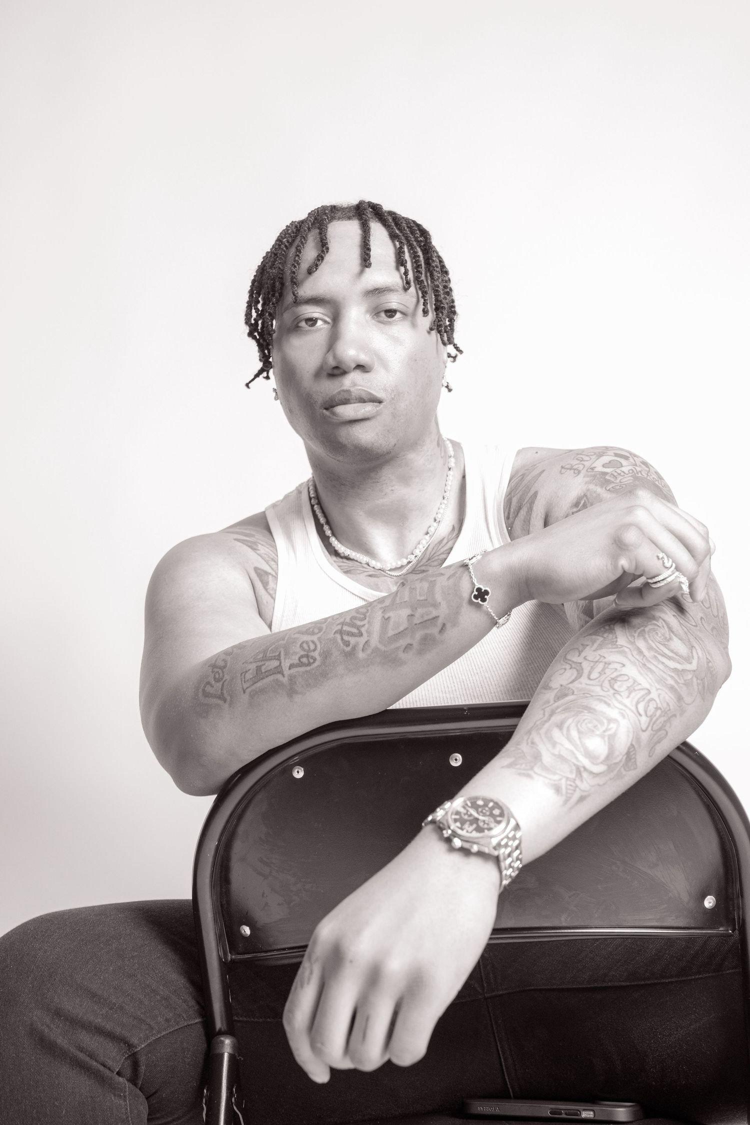 Black and white portrait showing tattooed arms and braided hair styling.