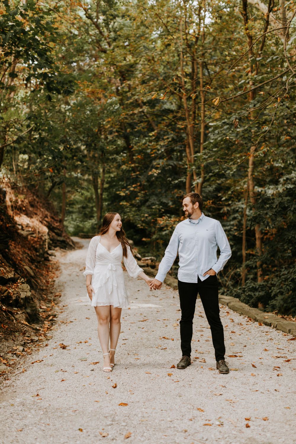 A couple walking hand in hand on a scenic forest path during their engagement photoshoot.