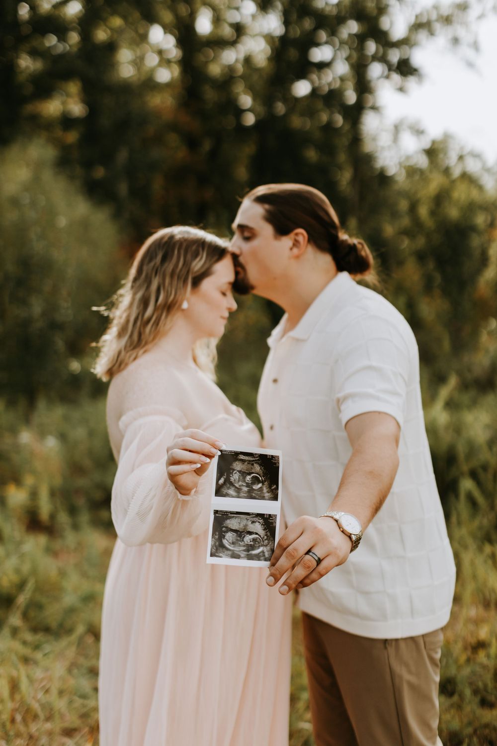 A couple shares an intimate moment while holding ultrasound photos during their maternity shoot.