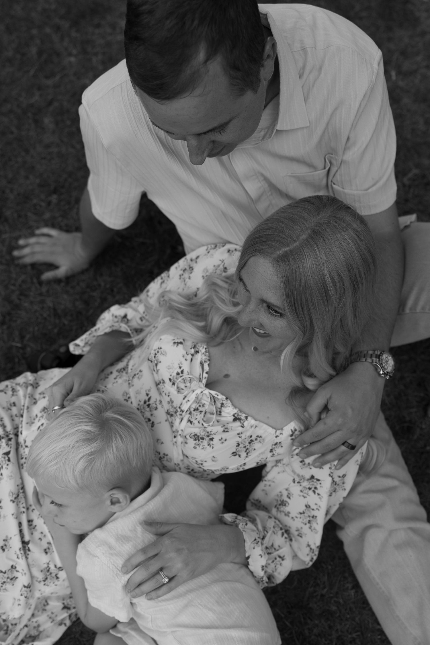 A tender black and white family moment captured while relaxing on grass outdoors.