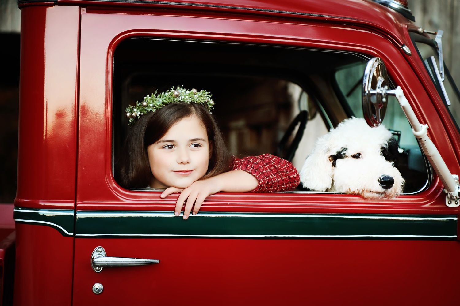 Young girl and white dog looking out window of vintage red truck with flower crown.