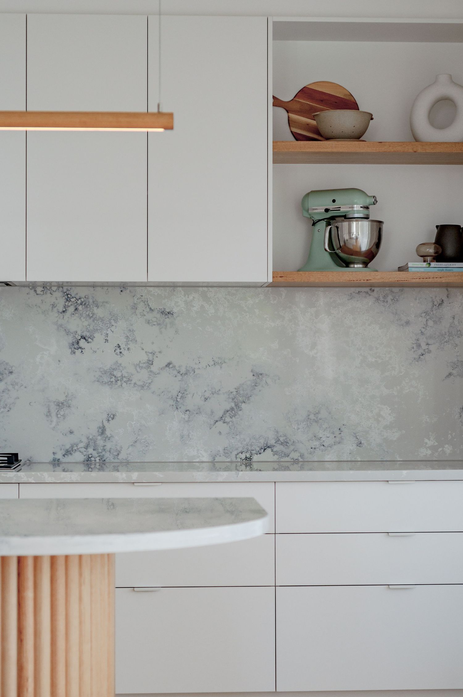 Modern kitchen featuring marble backsplash, wooden shelving, and mint green stand mixer.