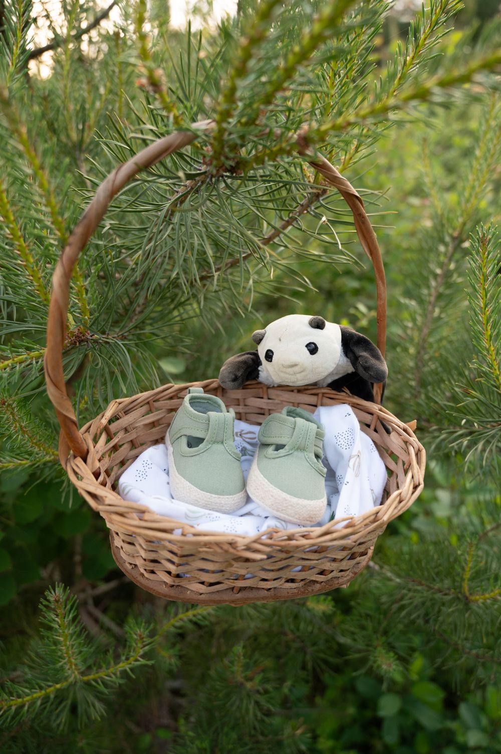 Détail d’un panier suspendu à un sapin avec des chaussons de bébé et un doudou à Barvaux