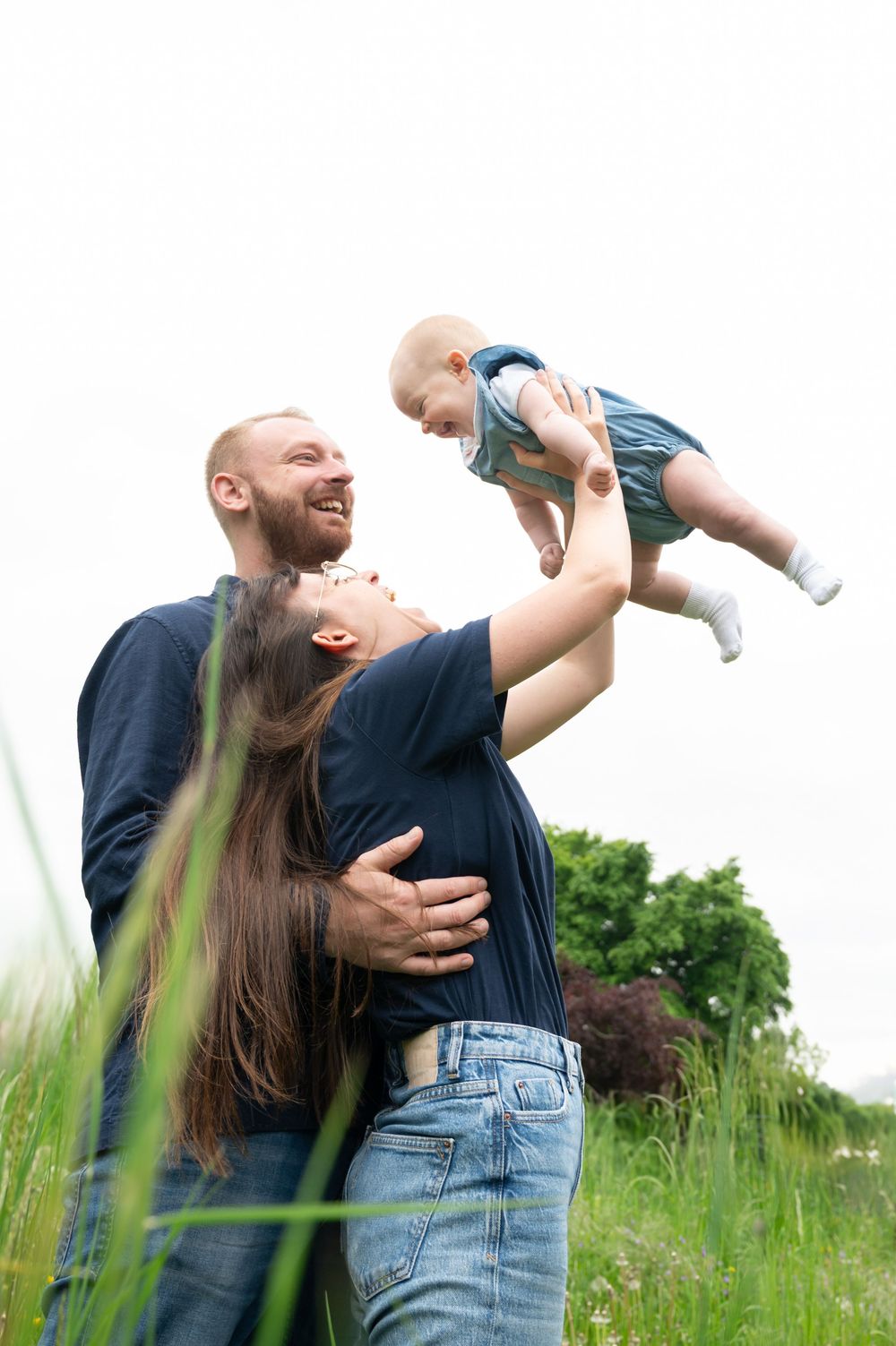 À Saint-Hubert, séance photo famille naturelle d’un couple jouant avec leur bébé, les bras levés pour le jeu de l’avion