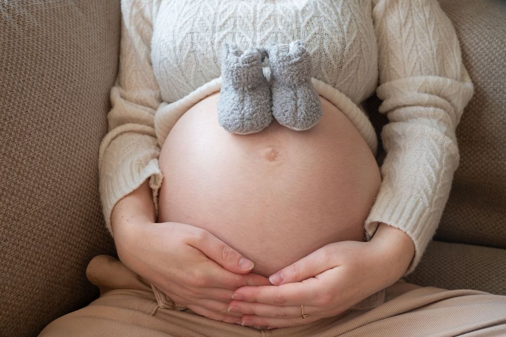 À Saint-Hubert, détail du ventre de la future maman avec des chaussons de bébé lors d’une séance photo grossesse