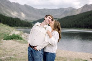 Couple sharing a romantic kiss by a mountain lake in Colorado, both wearing white shirts and jeans.