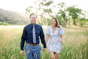 Couple walking and laughing together in a golden summer meadow at sunset wearing navy and white outfits.