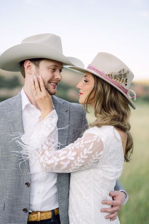 A romantic western-styled couple in cowboy hats share intimate moments in a rustic outdoor setting.