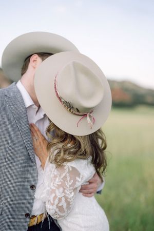 A tender moment between a couple wearing cowboy hats as they share an intimate embrace in a grassy meadow.
