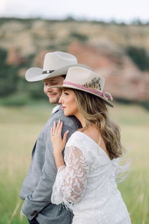 A couple in western attire embraces in a grassy field during a romantic photoshoot.