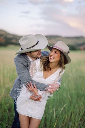 Romantic couple in cowboy hats sharing playful moments together in a sunlit meadow at sunset.