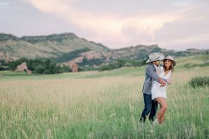 A couple embraces in a golden field with mountains and a pink sky visible in the distance.