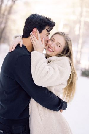A couple in winter attire embraces and shares tender moments in a snowy outdoor setting.