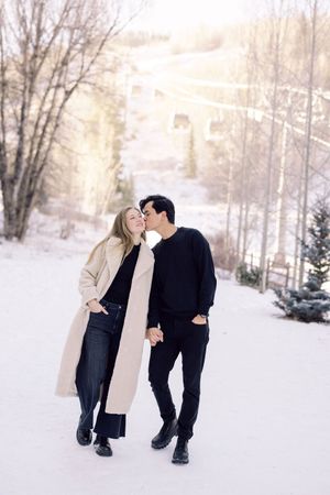 A couple shares tender moments together in a snowy winter landscape with bare trees in the background.