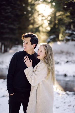 A couple shares tender moments in a snowy winter landscape wearing black and cream colored sweaters.
