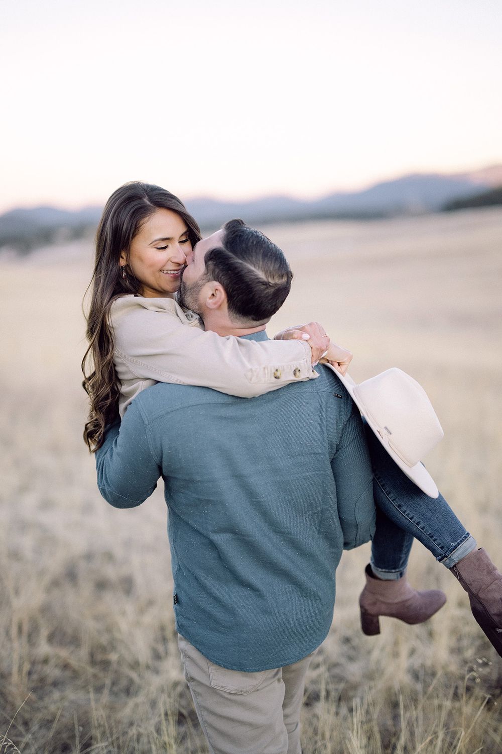 A playful moment between a couple as one carries the other through a field at sunset.