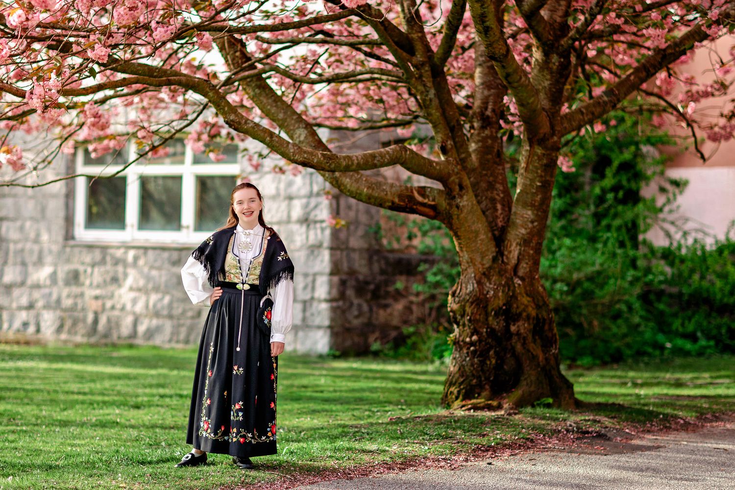 Smilende konfirmant i Frafjordbunad foran et blomstrende kirsebærtre på Dale i Sandnes, Rogaland.