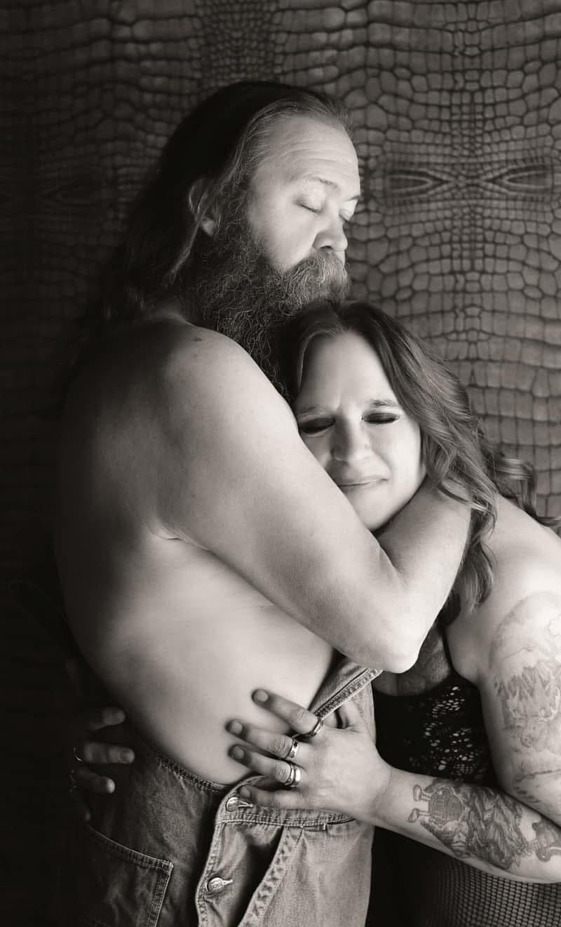 Black and white intimate portrait of a couple embracing against a textured background.