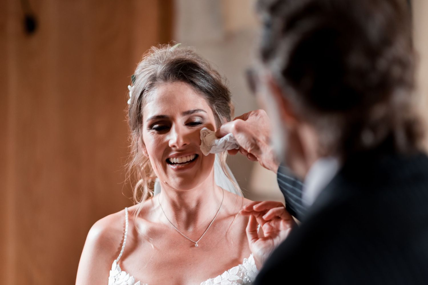 Emotional bride smiles and wipes away tears during a tender wedding moment.