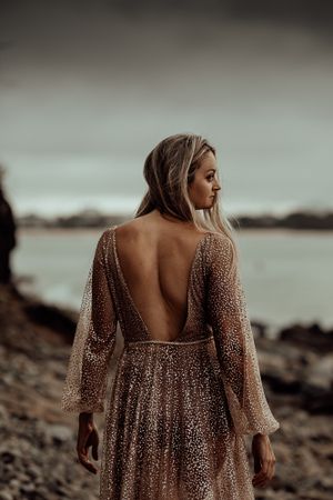 Backlit view of sparkly open-back dress on rocky coastline during golden hour.