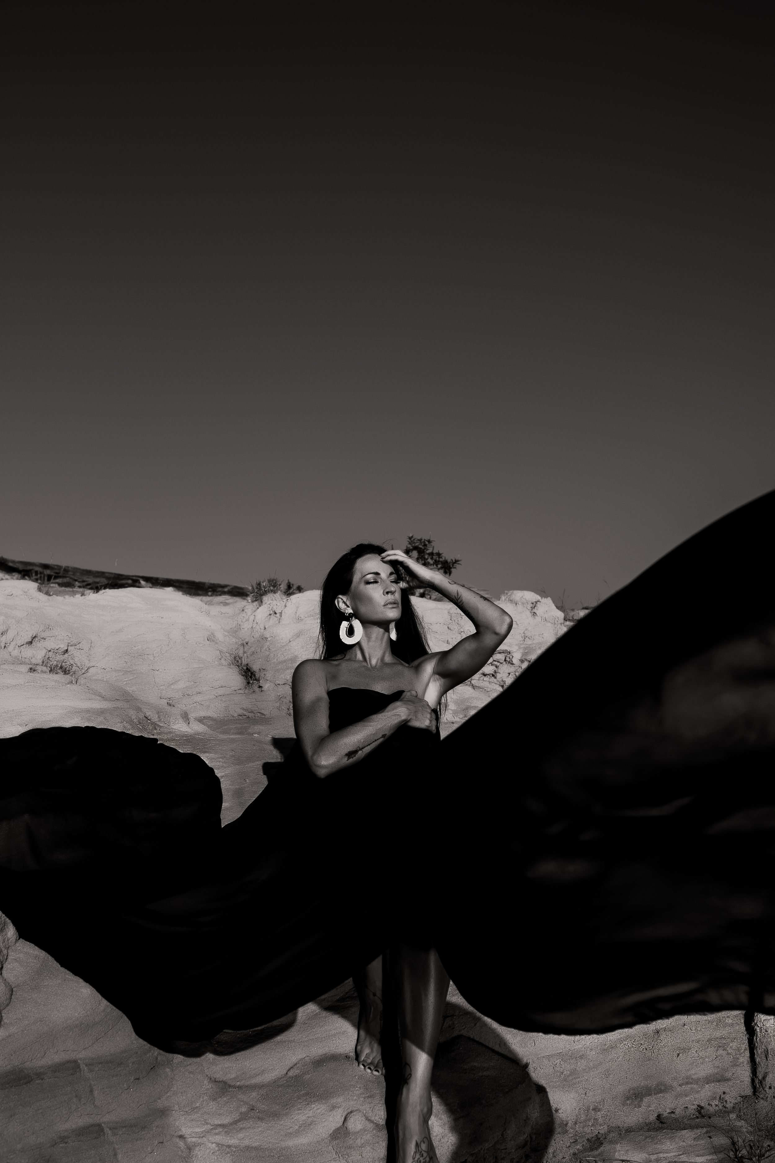 Dramatic black and white portrait with flowing fabric against desert landscape.