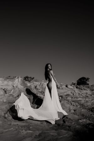 Elegant black and white photo of flowing white dress against rocky terrain.