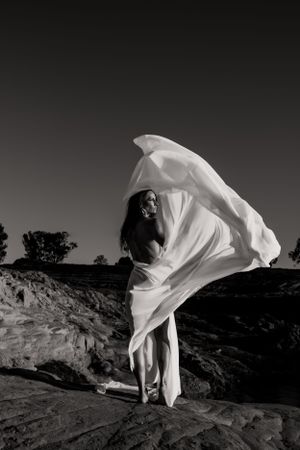 Ethereal portrait with billowing white fabric dancing in the wind on rocky landscape.