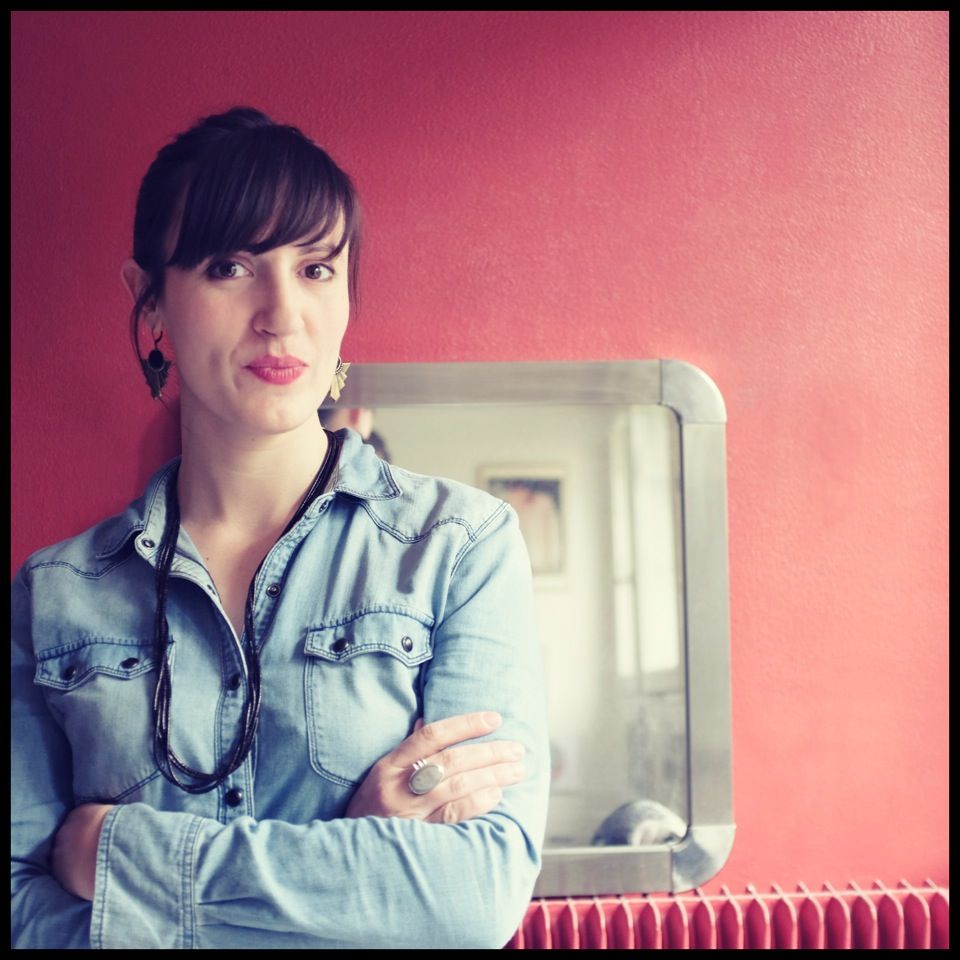 Portrait d'1 Femme meilleure photographe Le Havre chemise en jean bras croisés et sourire en coin regarde l'objectif devant un mur rouge