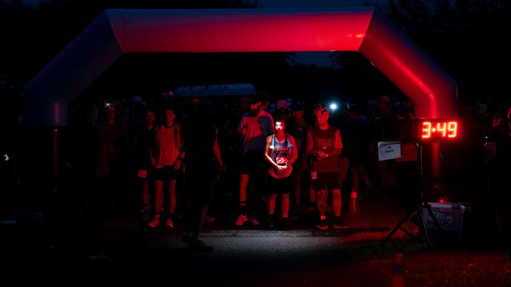 Silhouetted runners gather under red-lit archway at night race event.