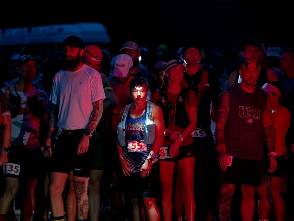 Group of runners illuminated by red lights during nighttime ultramarathon event.