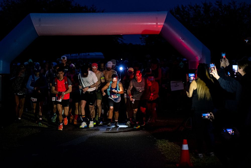 Trail runners gather before dawn with headlamps illuminating the starting area of a nighttime race event.