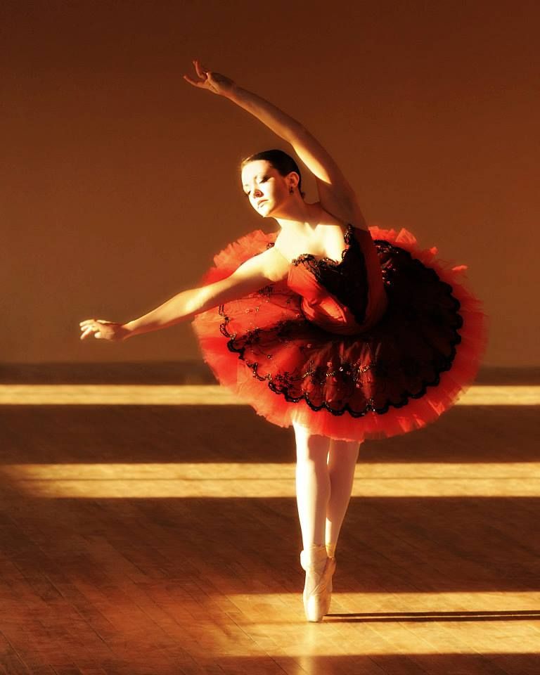 Ballet dancer in red tutu performing graceful pose on stage.