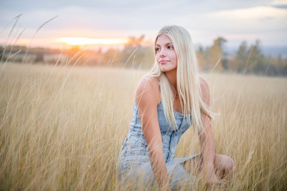 Woman in casual dress sitting in tall golden grass at sunset.