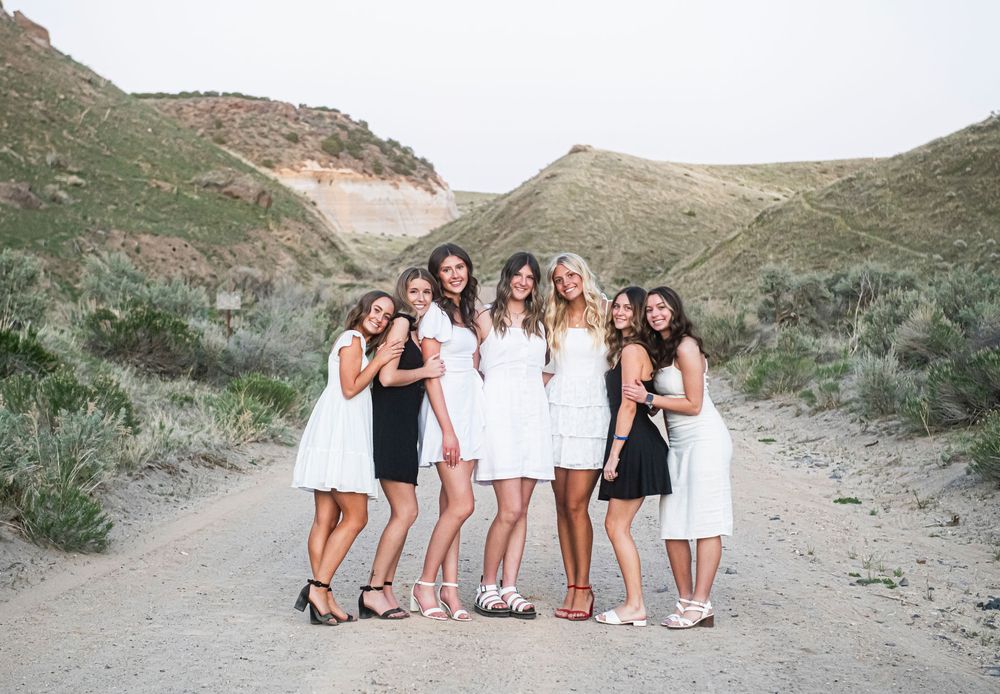 Group of friends in black and white dresses pose together on a scenic desert path between rugged hills.