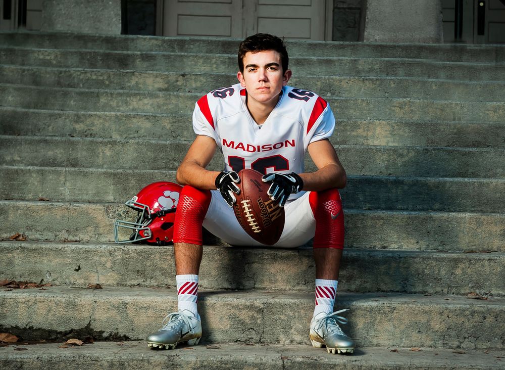 Football player in uniform sitting on stone steps with ball.