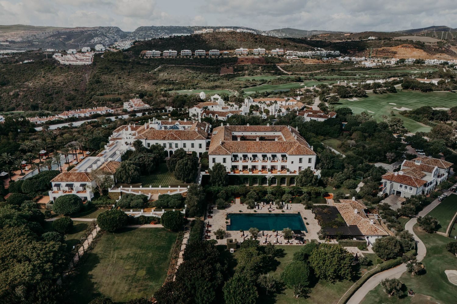 Aerial view of a luxury resort with white buildings and swimming pool nestled in rolling green hills of Portugal.