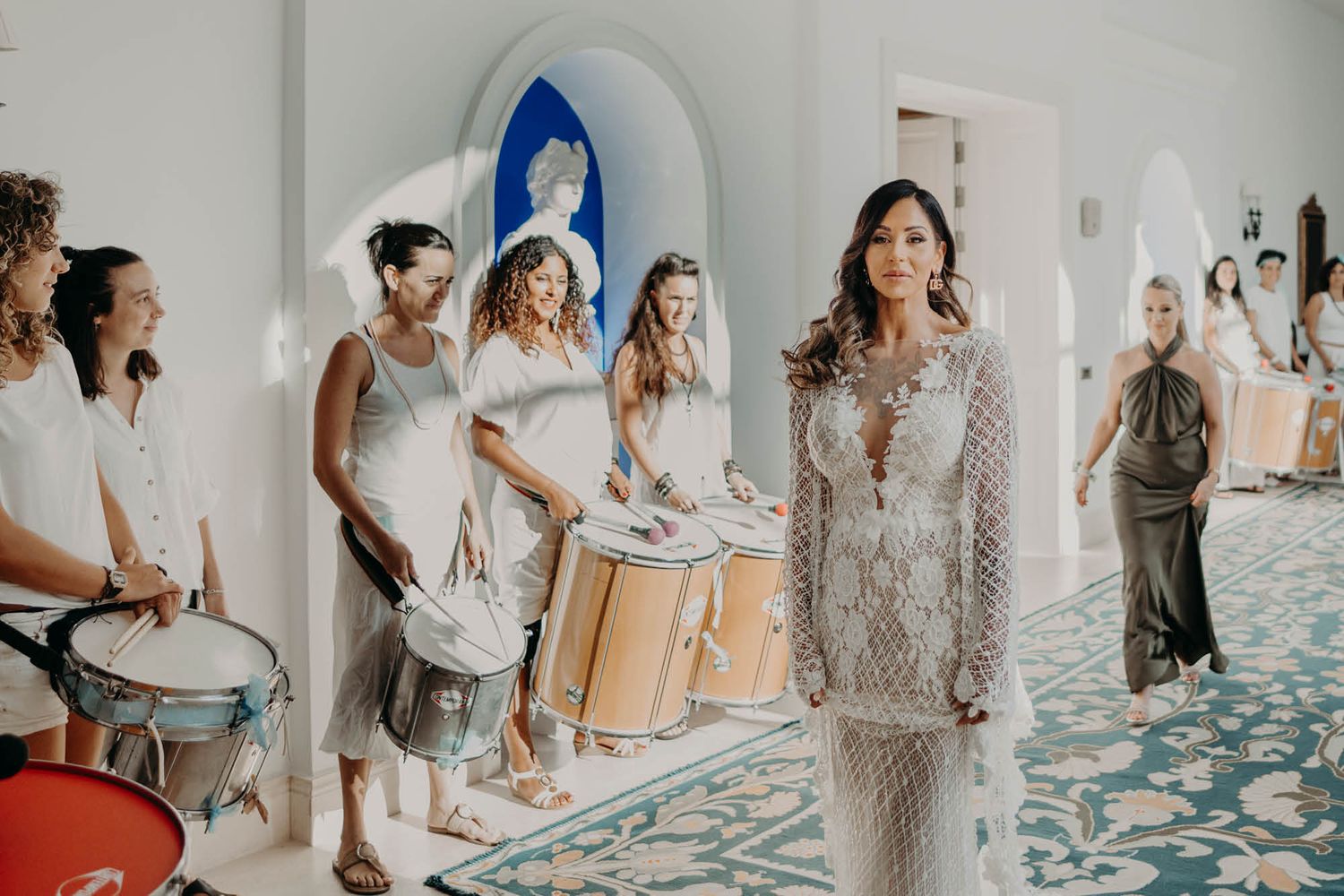 Musicians with drums create a festive atmosphere in a white Mediterranean-style interior space.
