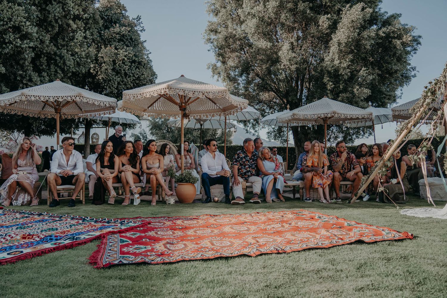 Outdoor wedding ceremony setup with boho rugs and rustic umbrellas creating a cozy atmosphere in a garden setting.
