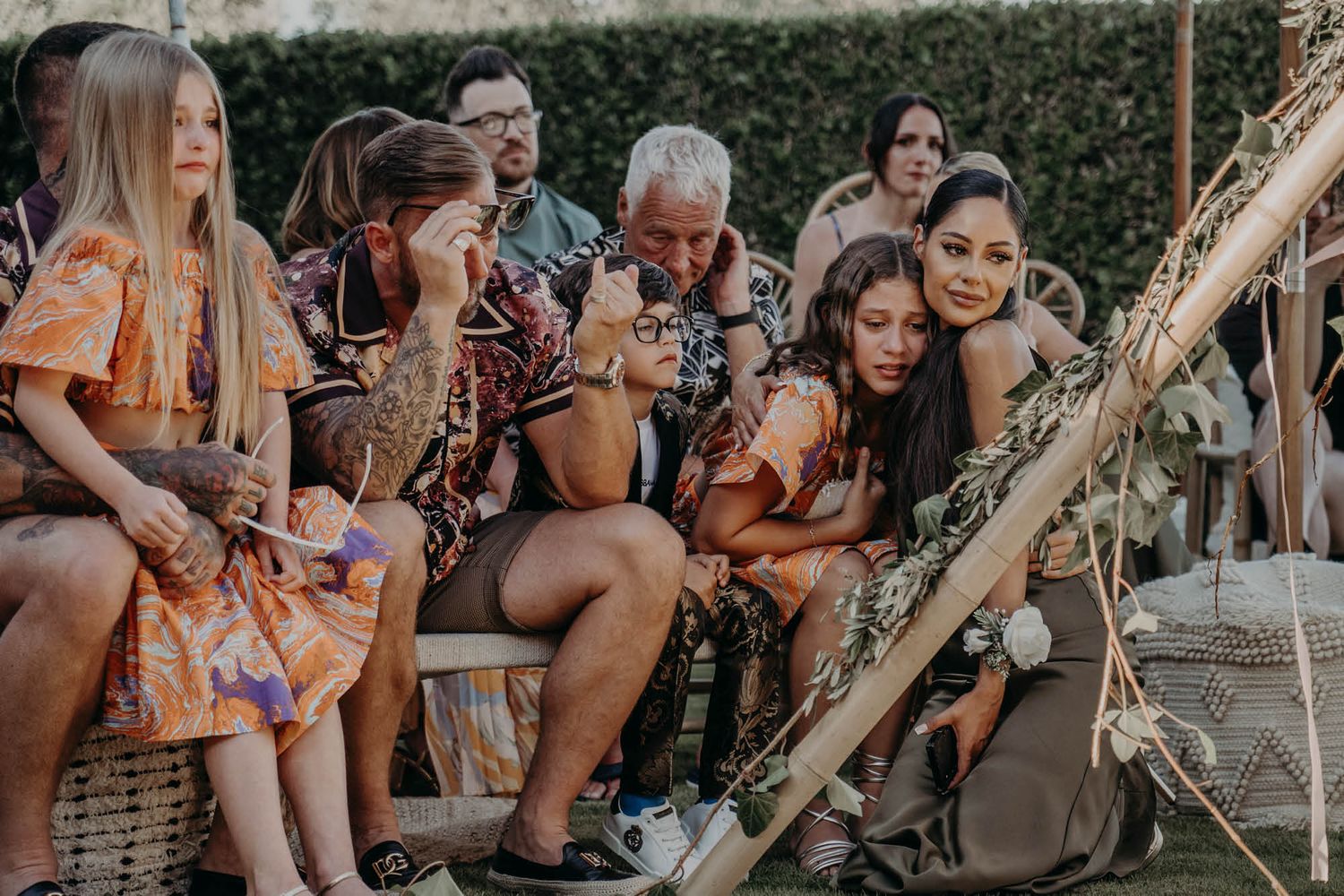 A group of people sitting together outdoors on wooden benches during a casual gathering at sunset.